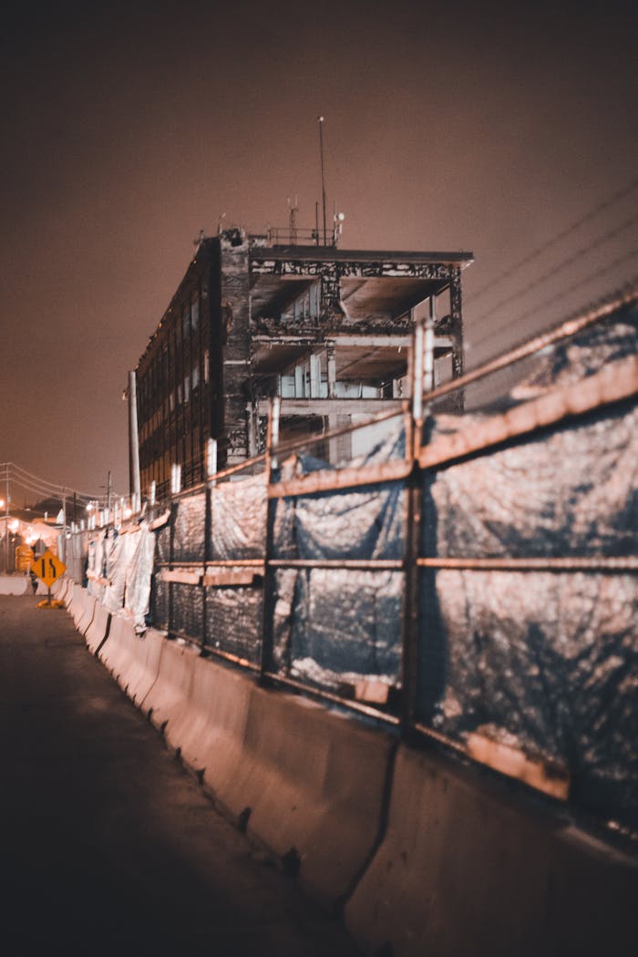 services-01 A broken building with concrete barriers and metal fences under a dark, night sky.