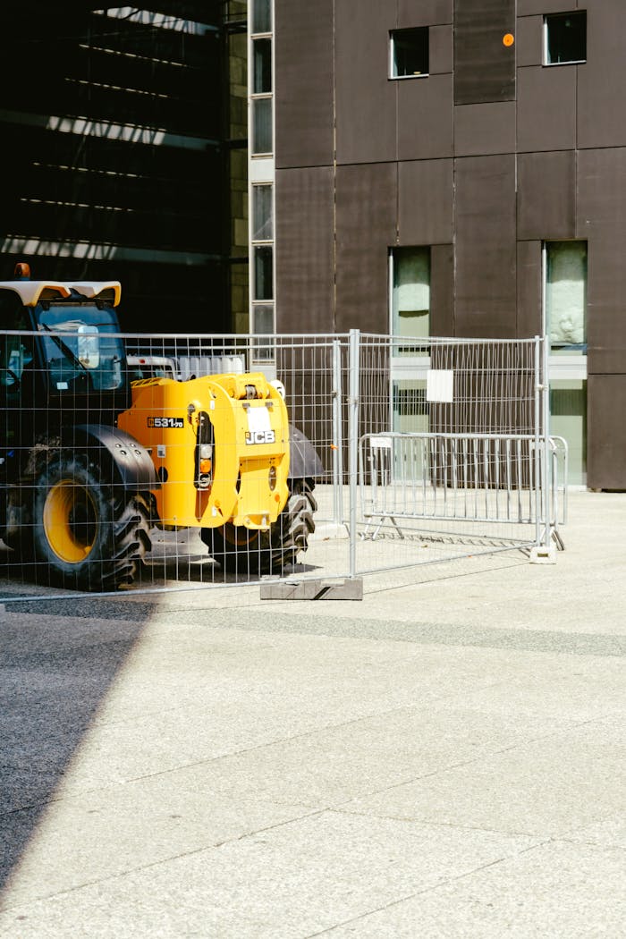 services-04 A yellow tractor parked behind a metal fence at an urban construction site.