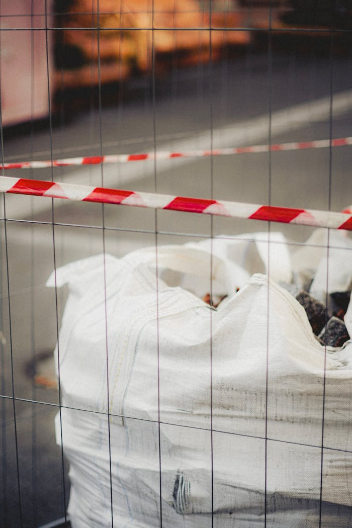 who-we-are Close-up of debris-filled sack at construction site enclosed by red and white tape.